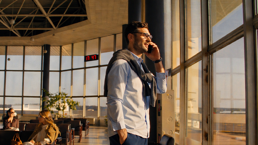 Persona en aeropuerto utilizando smartphone mientras sostiene una maleta promocionando tarifas de roaming para planes control.